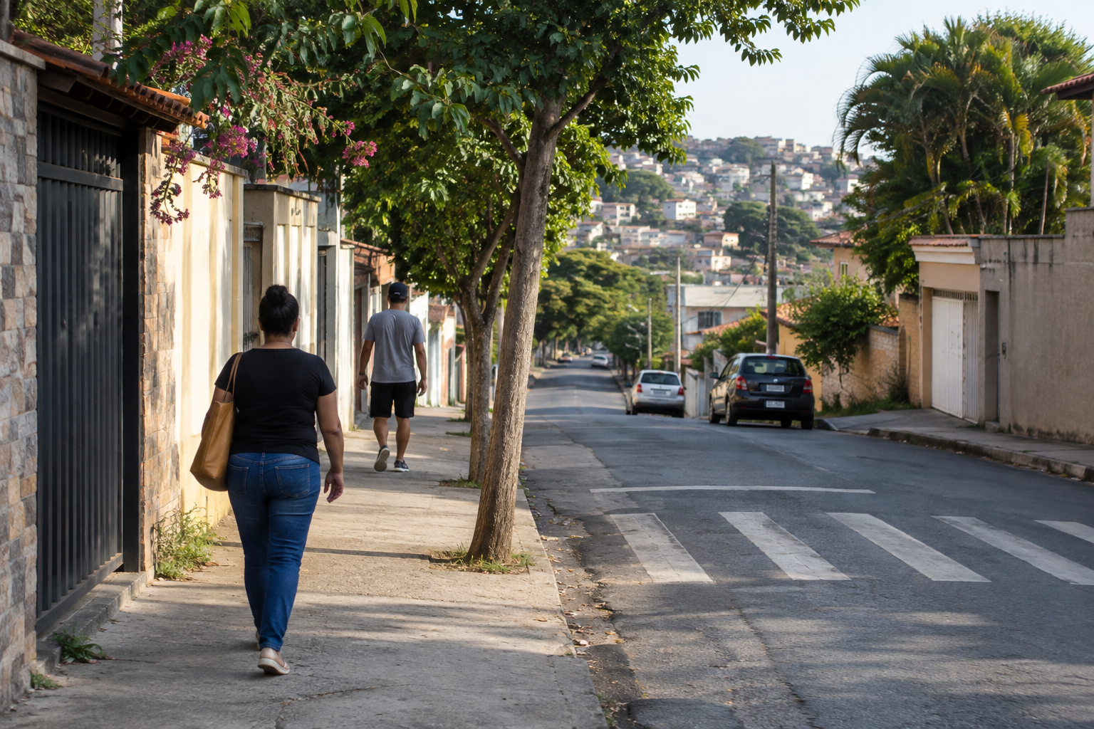 Calçada arborizada em bairro residencial, com pedestres vistos de costas e faixa de travessia ao fundo.