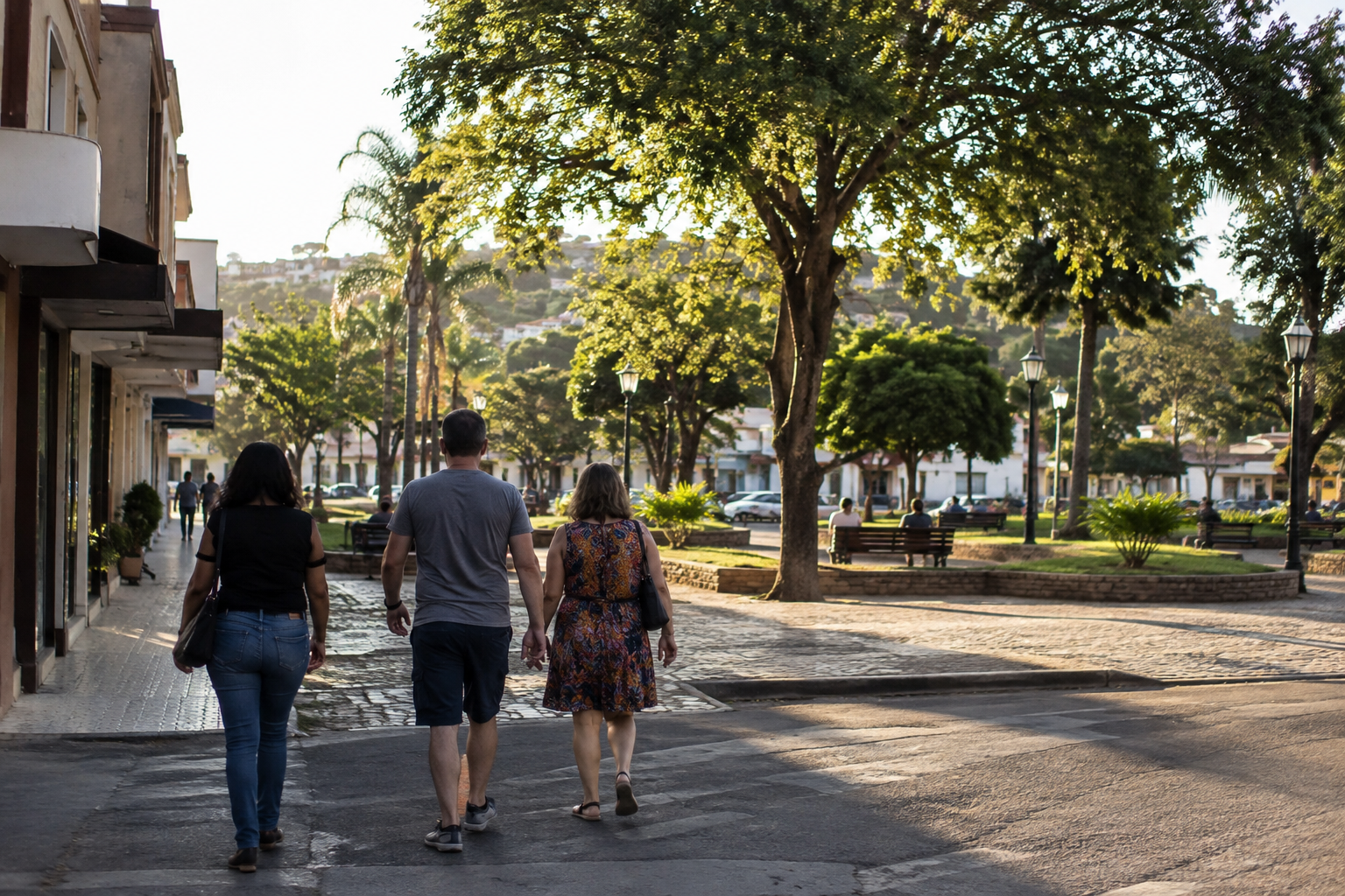 Pessoas vistas de costas caminham por rua urbana em direção a uma área arborizada de lazer em Minas Gerais.