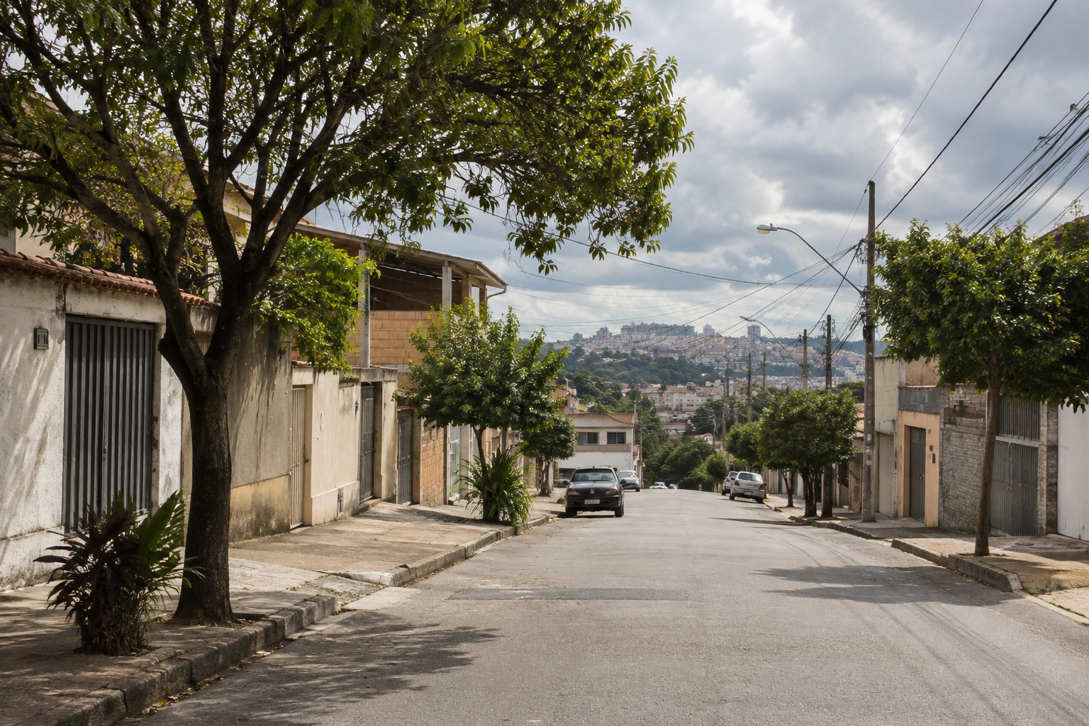 Rua residencial com árvores e construções baixas sob céu com muitas nuvens e aberturas de sol, em cenário urbano mineiro.